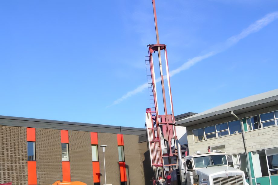 Une foreuse rouge sur camion devant un bâtiment de briques, mât levé, chantier géothermique