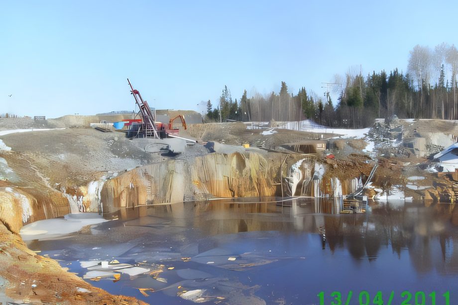 Une fosse remplie d’eau bleue entre des parois de roc, une foreuse en haut du talus