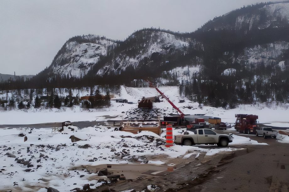 Foreuse au mât incliné sur un chantier enneigé de la Côte-Nord, camions et montagnes derrière