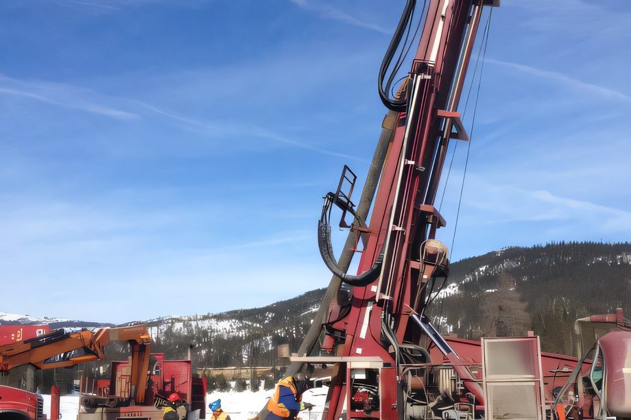 Le mât d’une foreuse rouge dressé contre un ciel bleu, montagnes de la Côte-Nord derrière