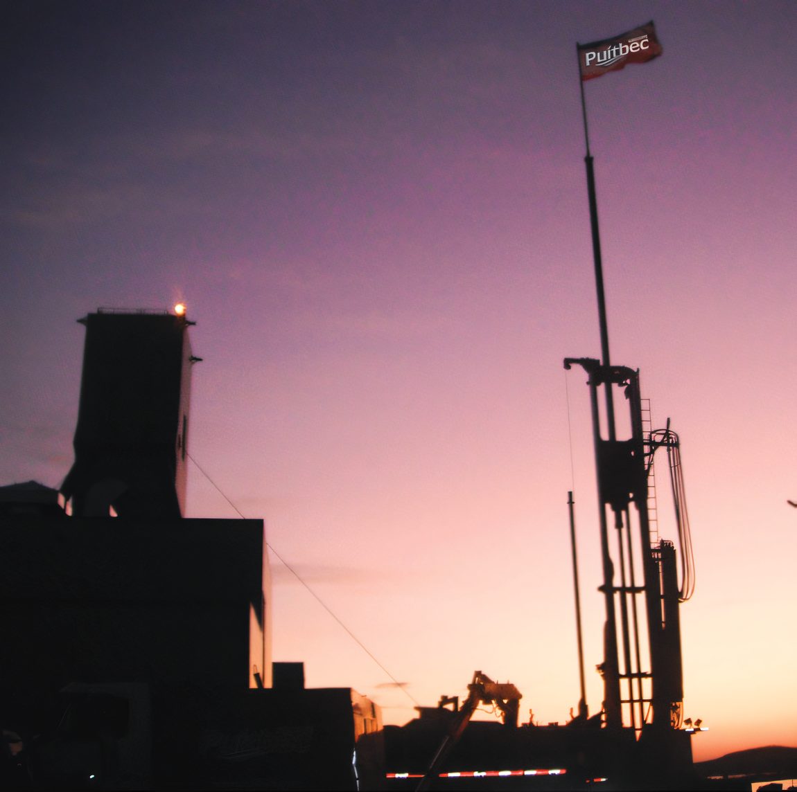 La silhouette d’une foreuse et d’un bâtiment au crépuscule, un drapeau Puitbec au sommet du mât
