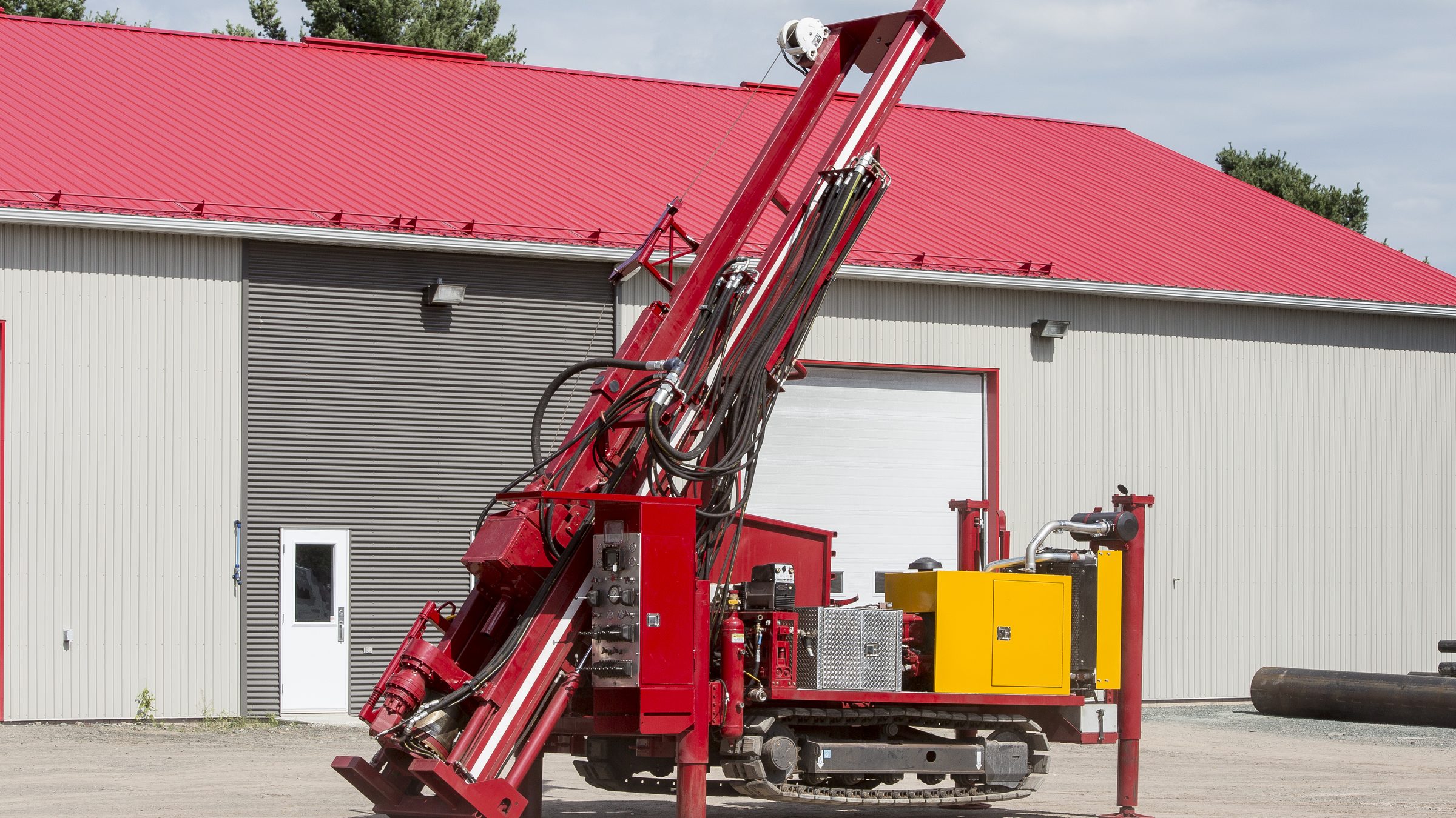 La foreuse sur chenilles Nordic Drill DRC-10-A, rouge à moteur jaune, mât incliné, devant le bâtiment au toit rouge de Groupe Puitbec