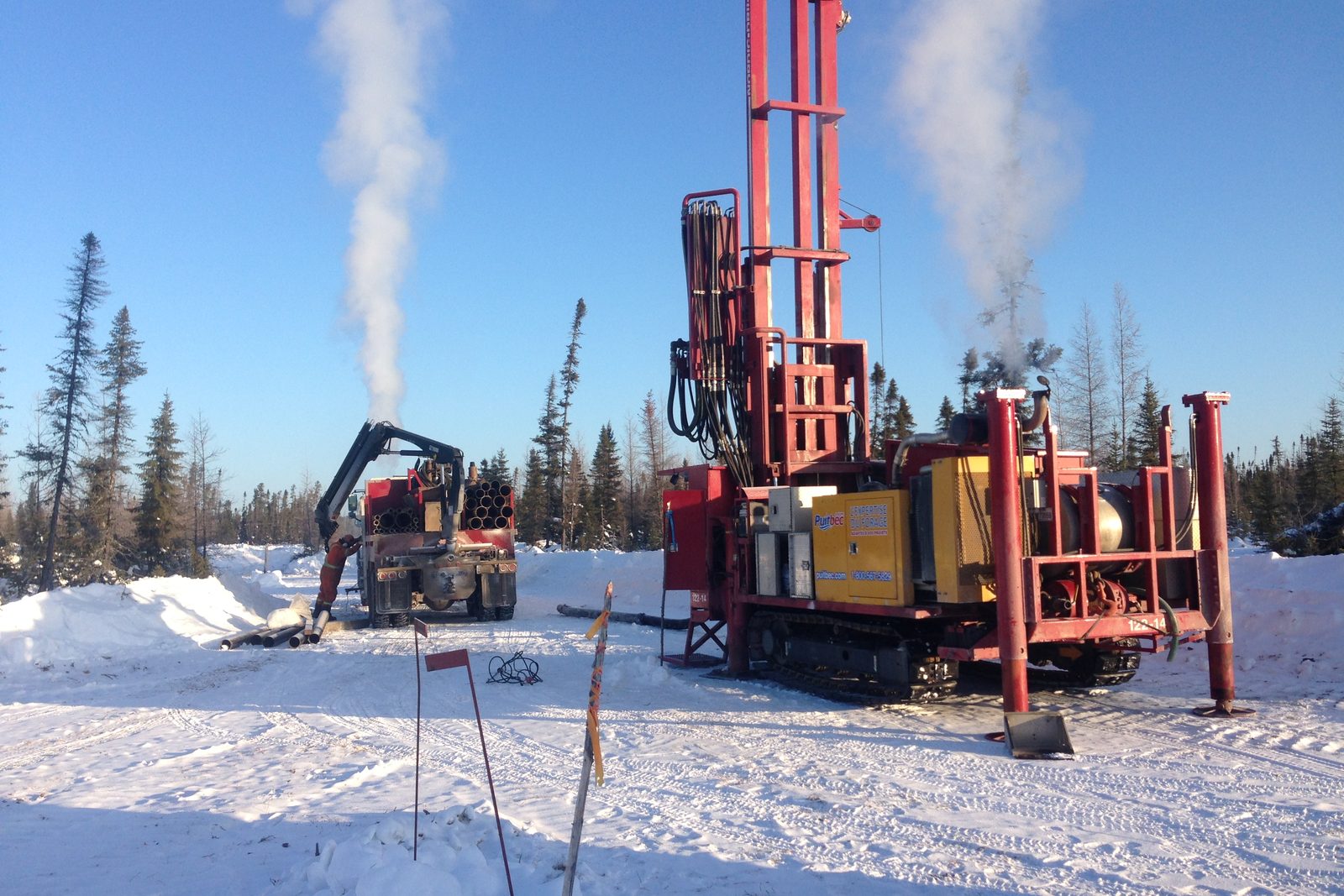Deux foreuses Puitbec en forage l’hiver dans une forêt d’épinettes, colonnes de vapeur dans le ciel bleu